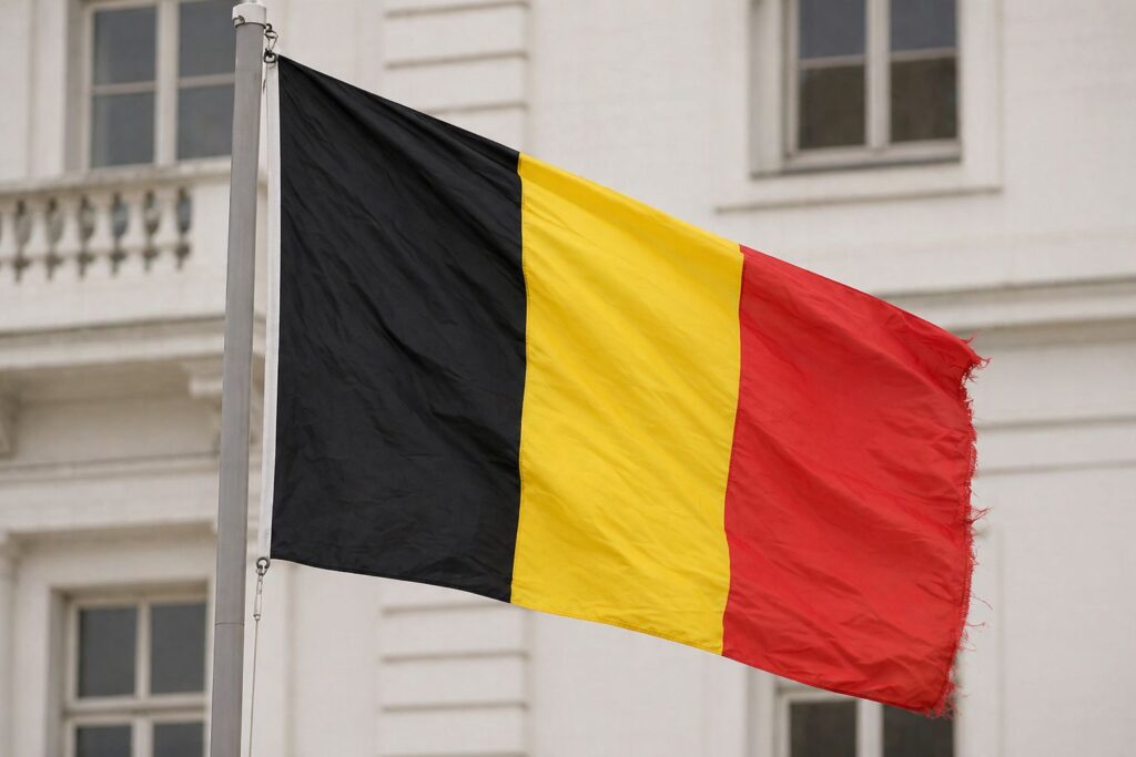 Flaga Belgii na maszcie powiewająca na wietrze na tle białego budynku